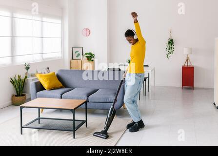 Happy young african woman dancing while vacuum cleaning at home Stock Photo