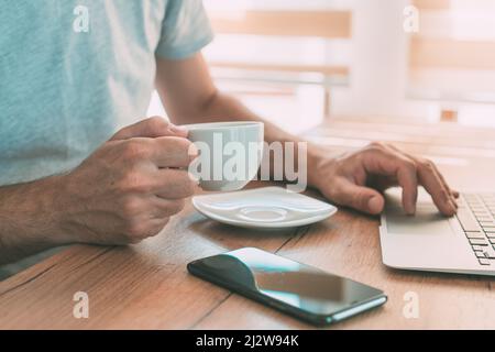 Freelancer is drinking coffee and working from home on laptop computer in the morning, selective focus Stock Photo