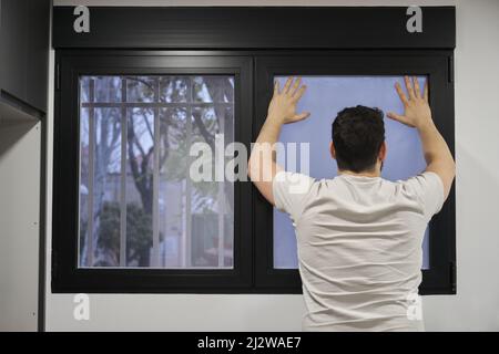 Man installing frosted window vinyl on wet window glass. Stock Photo