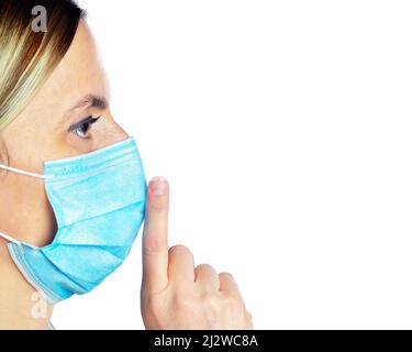 Woman wearing a face mask with her finger on her lips, keeping a secret or asking for silence Stock Photo