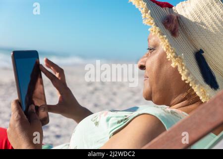 Retired senior african american woman using digital tablet while sitting on chair at beach Stock Photo