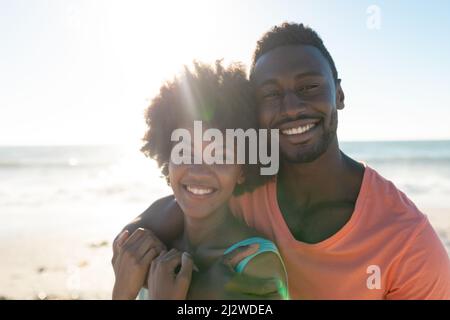 Back lit portrait of smiling african american couple enjoying summer holiday at beach on sunny day Stock Photo