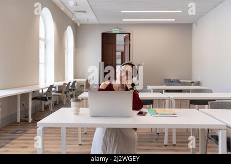 Tired Asian student girl in headphones doing gymnastics while studying online in modern classroom Stock Photo