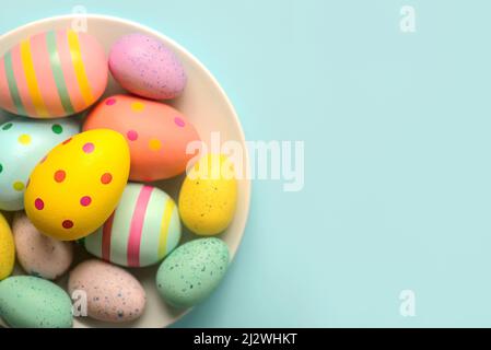 Happy Easter. Colored easter painted eggs in a bowl with copy space over blue background Stock Photo