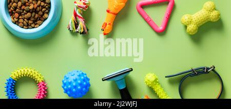 Pet shop wide banner design. Flat lay pet accessories, grooming equipment, bowl of dry food on green background. Stock Photo