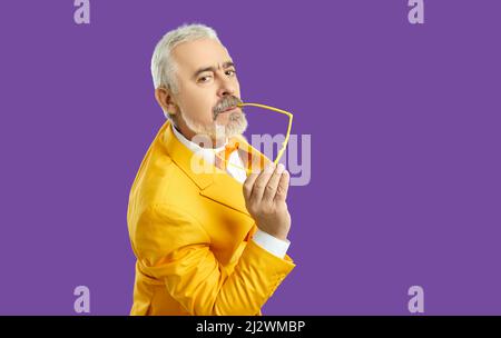 Portrait of handsome senior man in funky yellow suit posing isolated on purple background Stock Photo