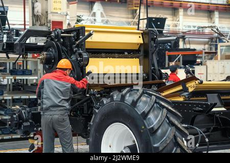 Worker assembles agricultural vehicle combine harvester in industrial factory workshop. Stock Photo