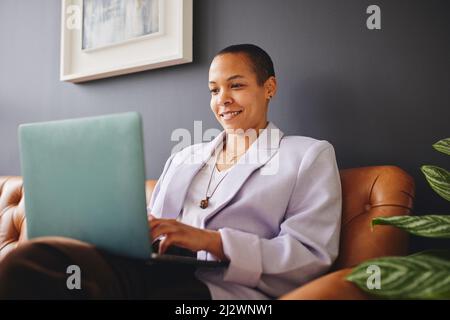 Portrait of cheerful multiracial LGBTQ mid adult woman using laptop on couch and smiling Stock Photo