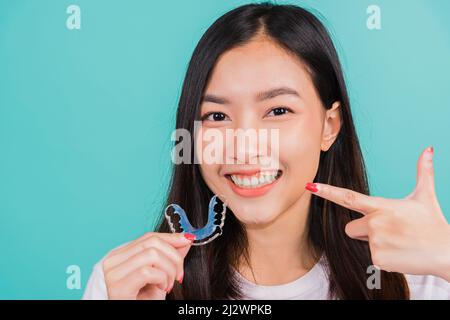 Female hold teeth retaining tools after removable braces, Portrait young Asian beautiful woman smiling pointing with finger silicone orthodontic retai Stock Photo
