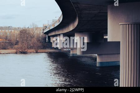 A concrete bridge viewed from below. The bridge turns to the left, the piers are visible. The bridge spans a river. The atmosphere is heavy. Stock Photo