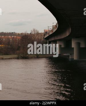 A concrete bridge viewed from below. The bridge turns to the left, the piers are visible. The bridge spans a river. The atmosphere is heavy. Stock Photo