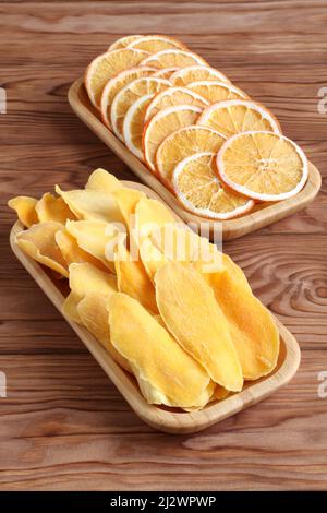 Dried pieces of mango and orange on a bamboo plates on a wooden table. Macro. Closeup. Stock Photo