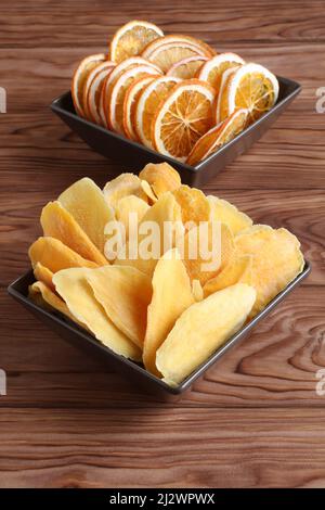 Dried pieces of mango and orange lying on a brown ceramic bowls on a wooden table. Macro. Closeup. Stock Photo
