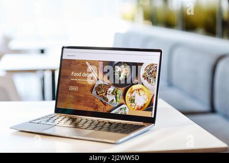 Background image of opened laptop with Food delivery website on table in food court or cafe interior, copy space Stock Photo