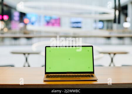 Background image of opened laptop with green screen chroma key on table in food court or cafe interior, copy space Stock Photo