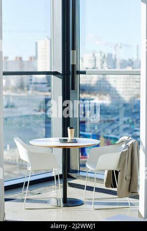 Vertical background image of minimal cafe setup against floor to ceiling windows with urban city skyline in background Stock Photo