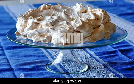 Meringue cake on a glass base placed on a table covered with a tablecloth. Stock Photo
