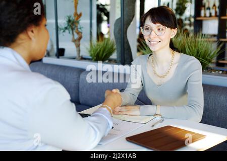 Portrait of smiling female entrepreneur shaking hands with partner during meeting at cafe table Stock Photo