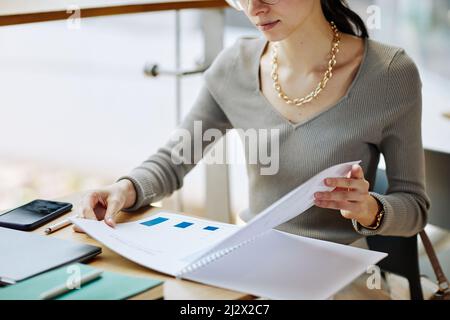 Cropped shot of elegant young woman reading marketing report while working at table in cafe, copy space Stock Photo