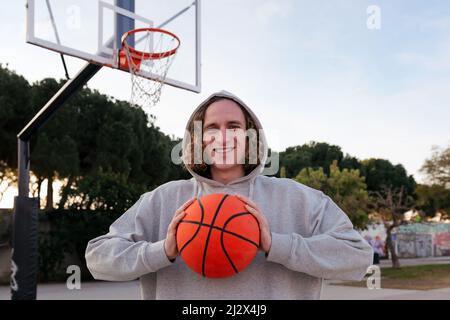 smiling young man on a basketball court holding a ball in his hands, concept of urban sport in the street, copy space for text Stock Photo