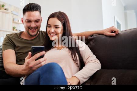We should go check out this new place. Shot of a man showing his girlfriend something on his cellphone while sitting at home. Stock Photo