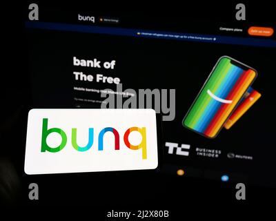 Person holding smartphone with logo of Dutch banking company bunq B.V. on screen in front of website. Focus on phone display. Stock Photo