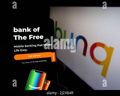 Person holding cellphone with website of Dutch banking company bunq B.V. on screen in front of business logo. Focus on center of phone display. Stock Photo