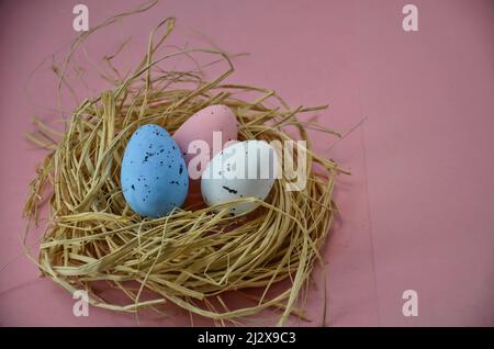 Three Easter eggs in straw on a pink background Stock Photo