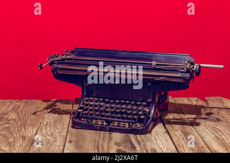 Pop art photography. Retro old, shabby typewriter standing on wooden table isolated on bright red background. Vintage, retro style. Stock Photo