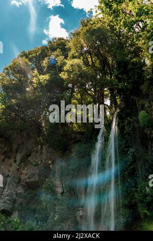 A vertical shot of a waterfall flowing through cliffs surrounded by trees Stock Photo