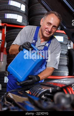 Skilled mature car mechanician changing motor oil in vehicle in auto repair shop.. Stock Photo