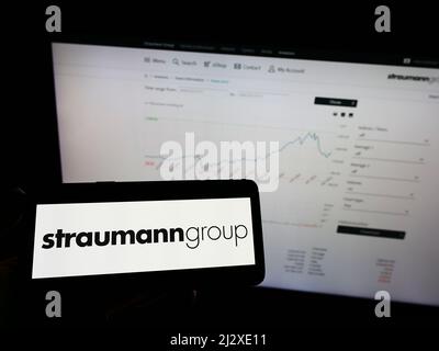 Person holding smartphone with logo of Swiss medical company Straumann Holding AG on screen in front of website. Focus on phone display. Stock Photo