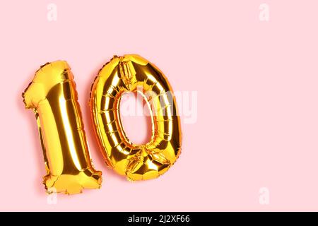 Number 10 golden balloons with copy space. Ten years anniversary celebration concept on a pink background. Stock Photo