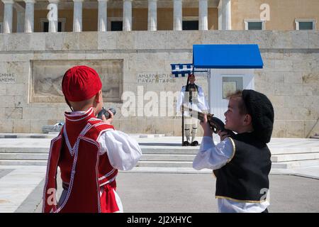 children in traditional Greek costumes look at the Soldier of the Presidential Guard, monument to the unknown Soldier ,Athens Greece March 25, 2022 Stock Photo