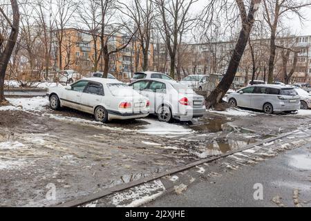 Russia, Vladivostok, March 21, 2022. Cars in a dirty parking after snow. Poor areas of city and infrastructure problems. Transportation and vehicles. Stock Photo