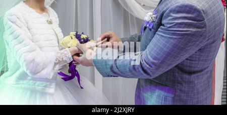 Wedding ceremony. The circumcised bodies of the newlyweds. The groom puts a wedding ring on his bride's finger. Stock Photo