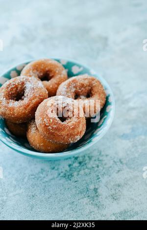 closeup of a blue ceramic bowl with some homemade rosquillas, typical spanish donuts sprinkled with sugar, on a stone surface Stock Photo