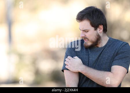 Stressed man scratching itchy arm complaining in nature