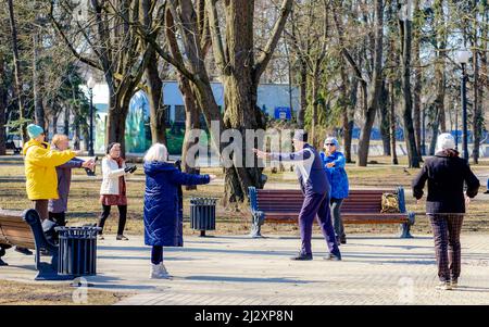 Minsk, Belarus - March 25, 2022: A group of old people doing breathing exercises in the park on a sunny day Stock Photo