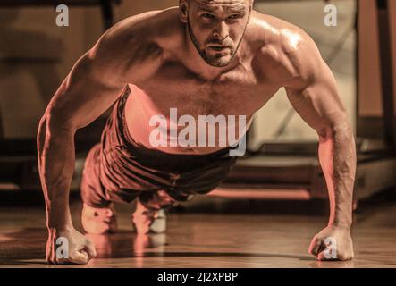 Man doing push-ups. Muscular and strong guy exercising. Slim man doing some push ups a the gym. Muscular man doing push-ups on one hand against gym Stock Photo
