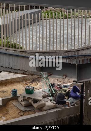 Bangkok, Thailand - Apr 02, 2022 : Exhausted tired two construction workers relaxing and fall asleep during working break on the mat under the bridge Stock Photo