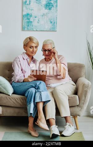 Vertical portrait of young woman helping senior mother using digital tablet and online services Stock Photo
