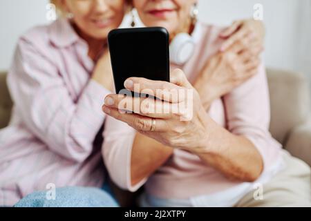 Close up of unrecognizable senior woman holding smartphone with daughter embracing her Stock Photo