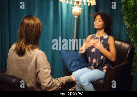 African-American young woman smiling while sitting in psychologist office. Female psychotherapist offering client to take test to determine cause of a Stock Photo