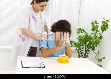 Crying upset mixed race nurse or afro american doctor with problems having stress breakdown at work. Colleagues comforting her. Stock Photo