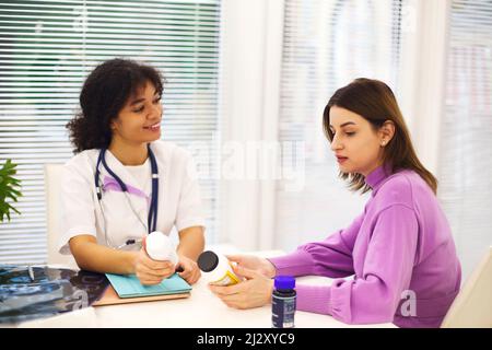 Beautiful young mixed race female doctor with pregnant patient in front of attendee, pill jar holder and written prescription on form. Medicine and ph Stock Photo