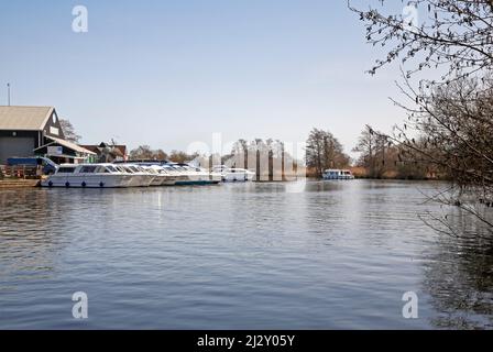 A boatyard by the River Bure on the Norfolk Broads with passing cruiser downstream of The Ferry Inn at Horning, Norfolk, England, United Kingdom. Stock Photo