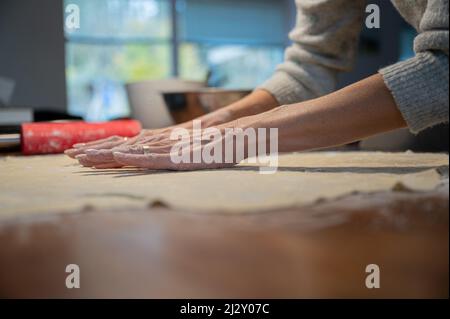 Low angle view of female hands stretching rolled pastry dough for strudel on a domestic dining table. Stock Photo