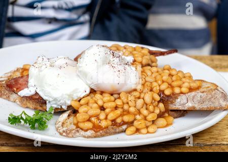 A healthier traditional english breakfast meal of beans on toast. It’s served with sour dough bread and the eggs are poached rather than fried Stock Photo