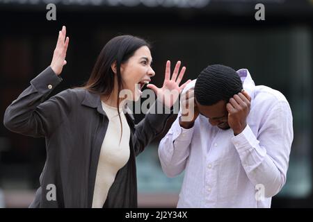 Angry woman scolding to a scared man in the street Stock Photo